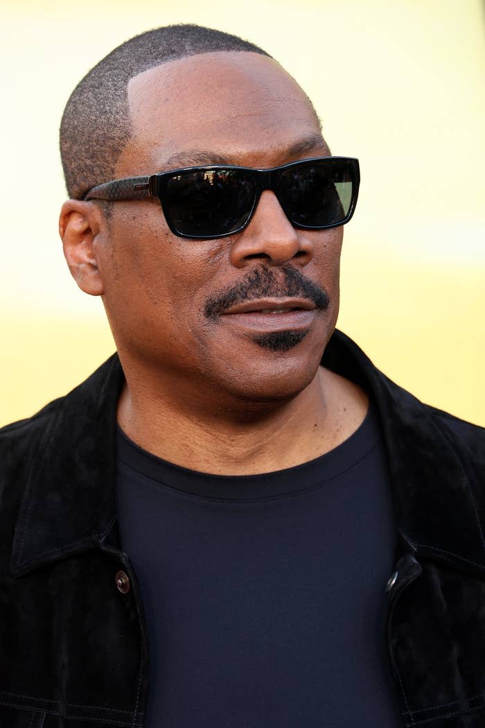 Eddie Murphy wears a black jacket and sunglasses at an event