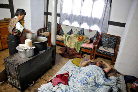 Farmer Ap Daw (R), 43, talks on his mobile phone as his son Sonam Tshering, 13, lies on a couch and his mother Aum Sangay, 68, heats water at their home in the Phobjikha Valley, Bhutan, December 15, 2017. "Children are spending more time on their mobile phones and not studying," said Daw who also bemoans the rising mounds of trash by the highway. REUTERS/Cathal McNaughton