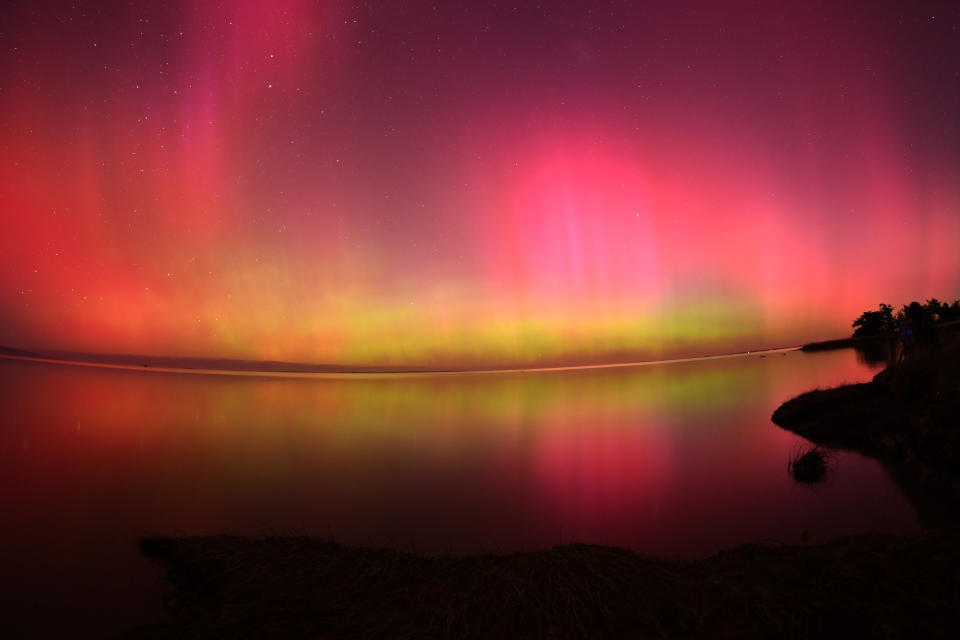 Der Himmel ist voller Vorhänge aus rotem Licht mit leicht gelben Farbtönen am Horizont, die sich im Wasser darunter spiegeln.