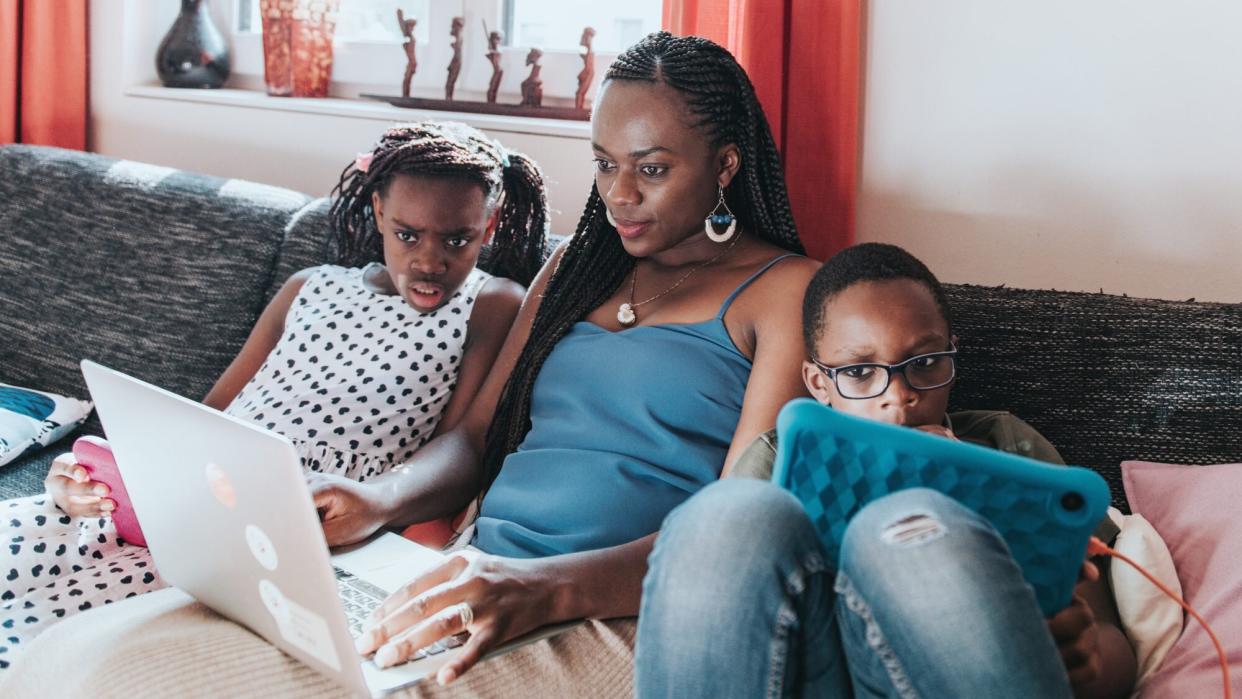 How to Balance Remote Work and Distance Learning: Mom sitting with her kids on the couch looking at computer