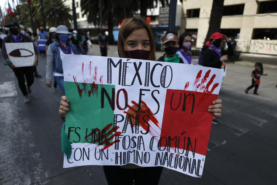 En esta imagen de archivo, una manifestante muestra un cartel con la frase "México no es un país, es una fosa común con un himno nacional" durante una marcha por el Día Internacional de la Mujer, en Ciudad de México, el 8 de marzo de 2021. Mujeres de todo el mundo exigirán igualdad salarial, derechos reproductivos, educación, justicia y otras necesidades esenciales durante las manifestaciones para conmemorar el Día Internacional de la Mujer el 8 de marzo. (AP Foto/Rebecca Blackwell, archivo)