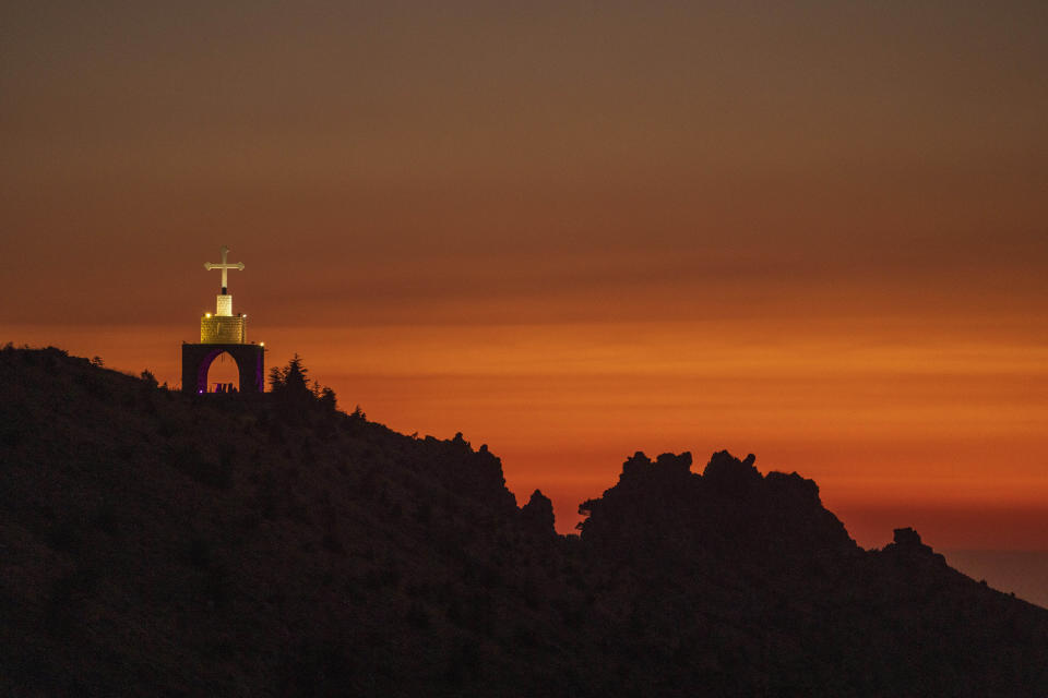 A Cross on a cliff overlooking the sunset over the scenic Kadisha Valley, a holy site for Lebanon's Maronite Christians, in the northeast mountain town of Bcharre, Lebanon, Friday, July 21, 2023. For Lebanon's Christians, the cedars are sacred, these tough evergreen trees that survive the mountain's harsh snowy winters. They point out with pride that Lebanon's cedars are mentioned 103 times in the Bible. (AP Photo/Hassan Ammar)