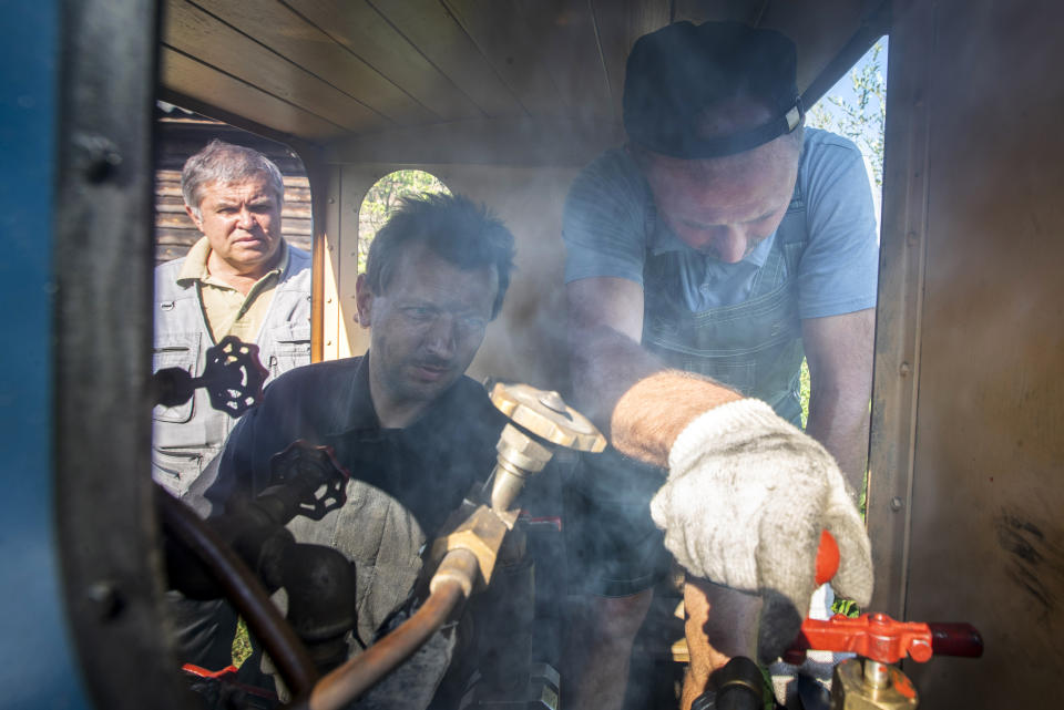 Pavel Chilin's assistants Sergei Terekhov, center, and Vadim Gukov drive a locomotive on Pavel Chilin's personal railway in Ulyanovka village outside St.Petersburg, Russia Sunday, July 19, 2020. It took Chilin more than 10 years to build the 350-meter-long miniature personal narrow-gauge railway complete with various branches, dead ends, circuit loops, and even three bridges. (AP Photo/Dmitri Lovetsky)