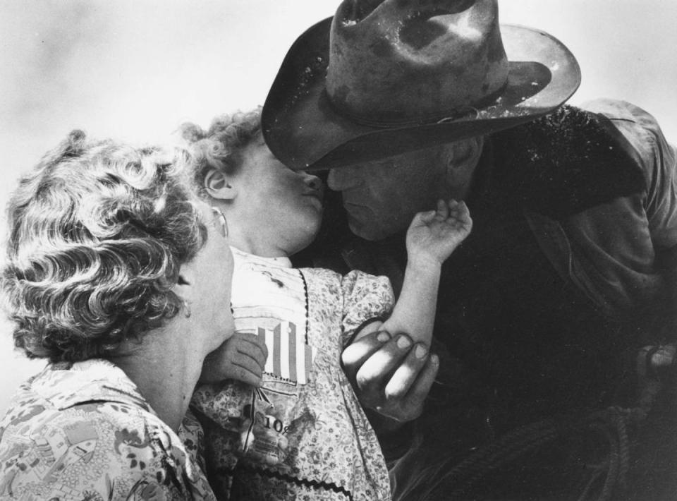 A black and white photo of a man in a cowboy hat kissing a small child held by a blonde woman.