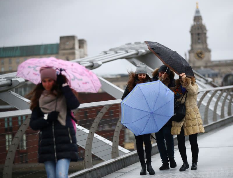People struggle with umbrellas as they walk across Millennium Bridge during storm Dennis in London