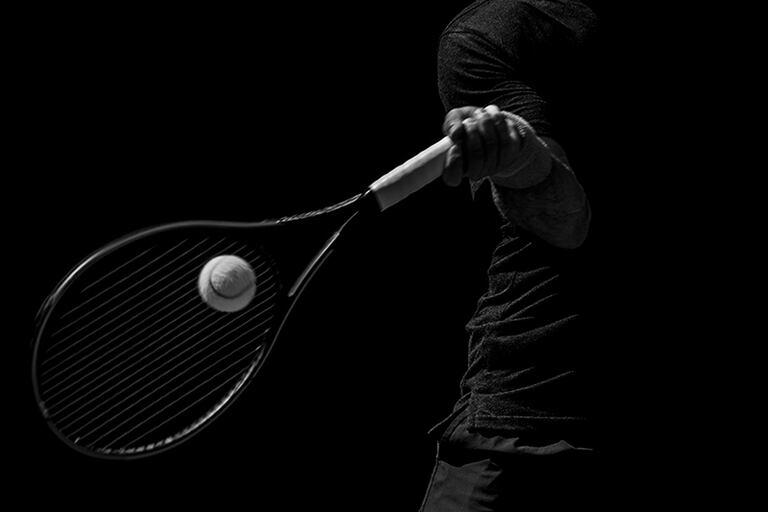 Male tennis player in action on the court on a sunny day. Black and white