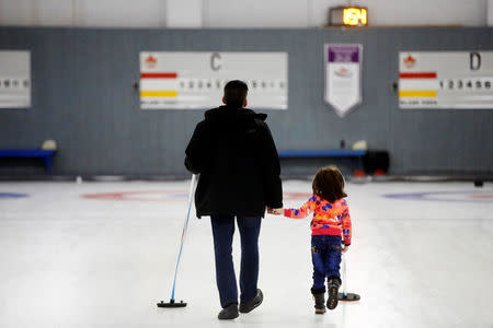 A father and daughter, who are refugees from Syria, walk the ice as they were introduced to the sport of curling at the Royal Canadian Curling Club during an event put on by the "Together Project", in Toronto, March 15, 2017. REUTERS/Mark Blinch