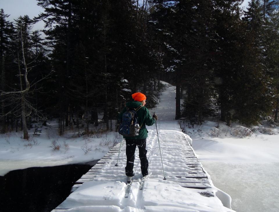 This December 2012 photo shows Lynn Dombek cross-country skiing over a bridge on the Lodge to Lodge trail between camps at the Appalachian Mountain Club’s backcountry wilderness lodge near Greenville, Maine. In winter, visitors can reach the lodges and cabins only by cross-country skiing in. (AP Photo/Donna Lawlor)