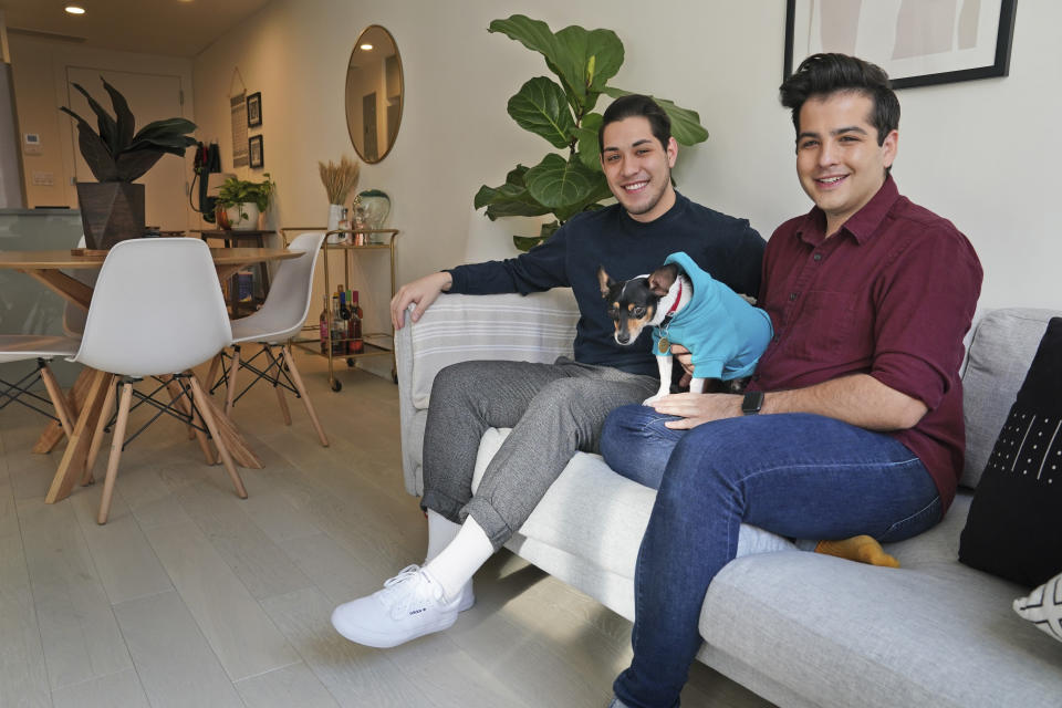 In this Monday, Nov. 25, 2019 photo, Zachariah Mohammed, left, Pete Mancilla, and their dog Remy pose for a picture in their apartment in New York. Most of the furniture in their apartment, including the couch, the table and chairs, the side table and the bar cart, are rented. Furniture-rental startups and other companies are aiming to rent furniture to millennials who don't want to commit to big purchases or move heavy furniture and are willing to pay for the convenience. (AP Photo/Seth Wenig)