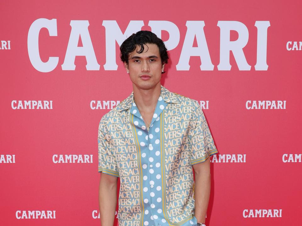 charles melton in a versace shirt and black pants, on a red campari branded carpet