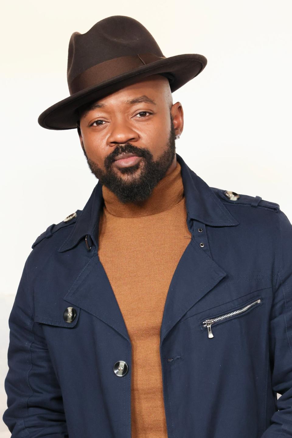 Brian in a hat, navy jacket, and tan sweater poses at an event