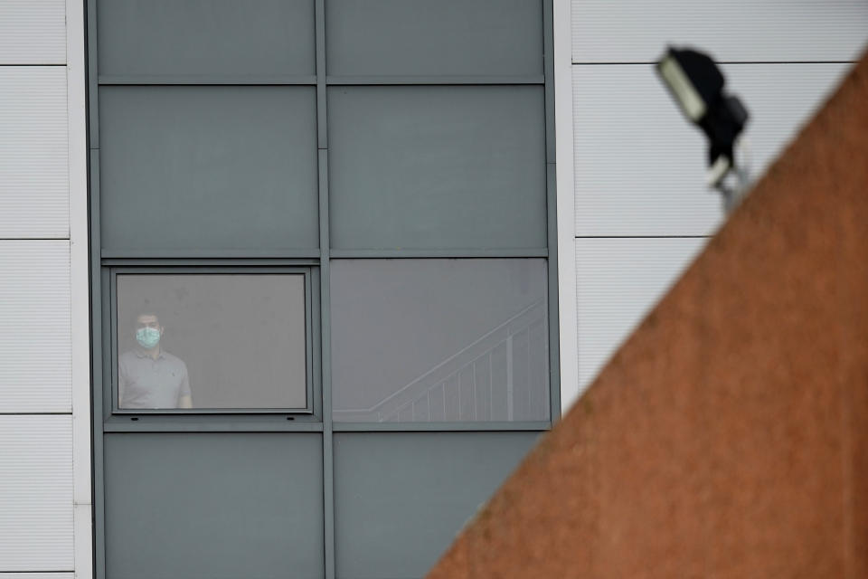 A person wearing a mask stands at a window of a staff accommodation block where British nationals recently flown back from China and at risk from the new virus are being quarantined, at Arrowe Park Hospital, on the Wirral, in Liverpool, England, Wednesday Feb. 5, 2020. Britain on Tuesday urged all of its citizens in China to leave the country because of the outbreak of a respiratory illness from a new virus, while Belgium became the latest nation to announce a confirmed case. (AP Photo/Jon Super)