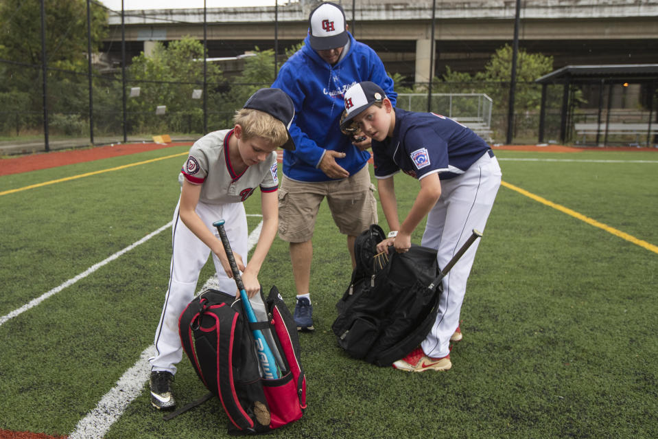 David Fox, center, with his sons Dewey, right. and Jimmy gather their equipment as they wrap up practicing baseball at a baseball field in northeast Washington, Friday, Aug. 23, 2019. David Fox and his wife, Mary Ann, have a rule for their sons, 11-year-old Dewey and 8-year-old Jimmy: They have to play a team sport. The kids get to choose which one. Dewey tried soccer and Jimmy had a go at flag football, but every spring and fall, their first choice is baseball. (AP Photo/Manuel Balce Ceneta)