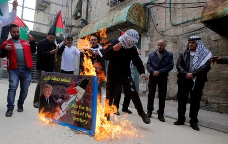 FILE PHOTO: Palestinian demonstrators burn a poster depicting U.S. President Donald Trump during a protest in Hebron in the Israeli-occupied West Bank