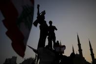 A demonstrator holds a Lebanese national flag as he sits atop a statue on Martyrs' square, as the Al-Amin mosque is seen in the background, during an anti-government protest in downtown Beirut