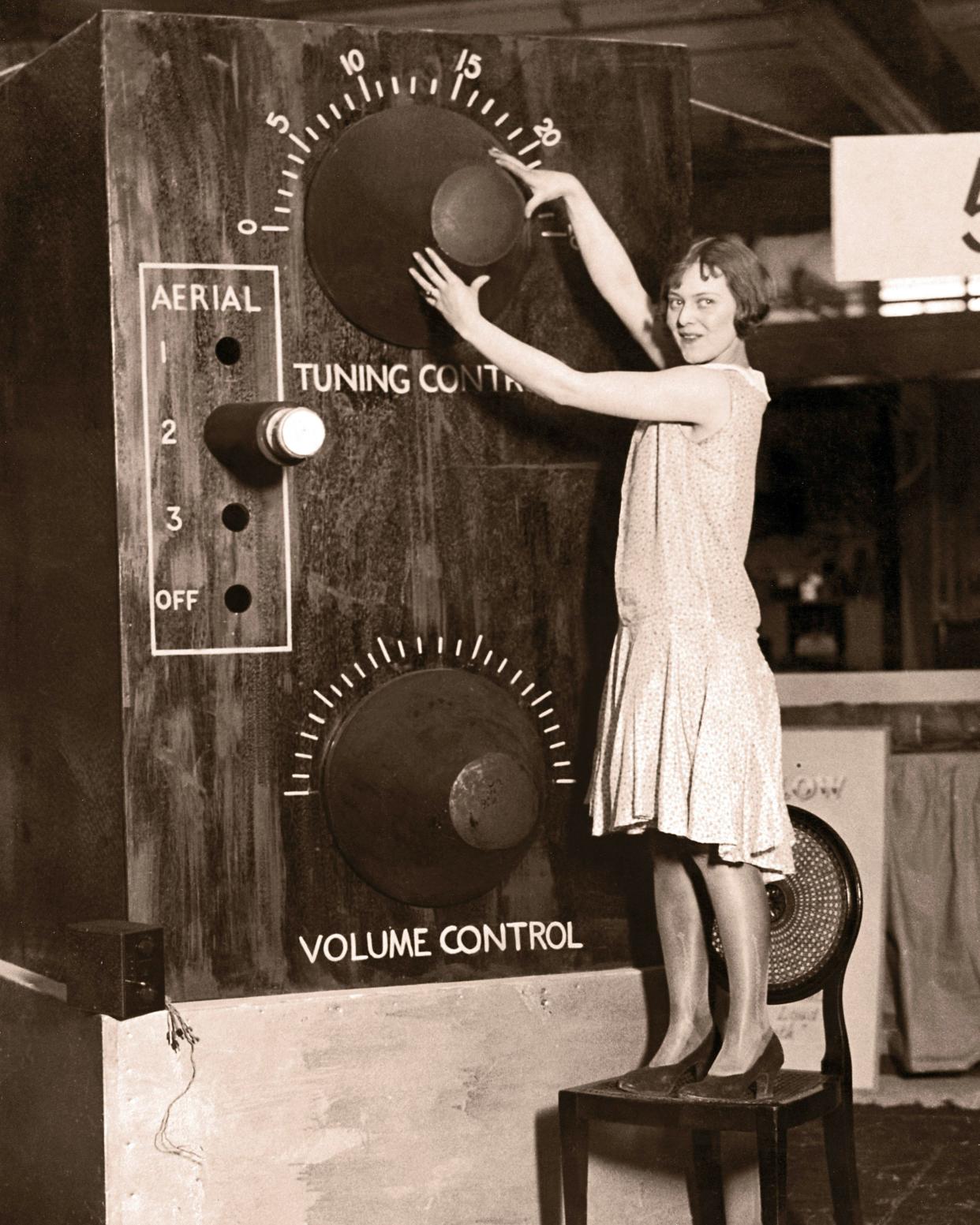 young woman, standing on chair, adjusting giant radio tuner