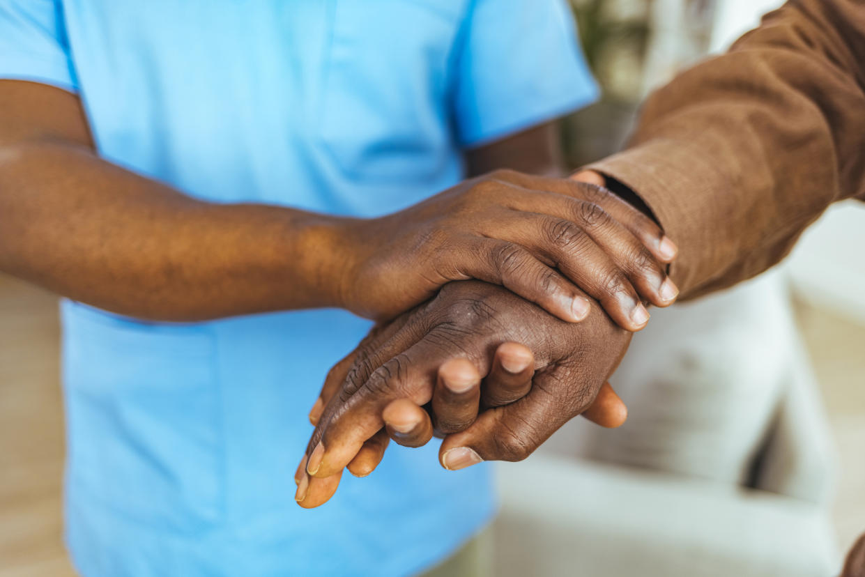 Home caregiver and senior man holding hands.