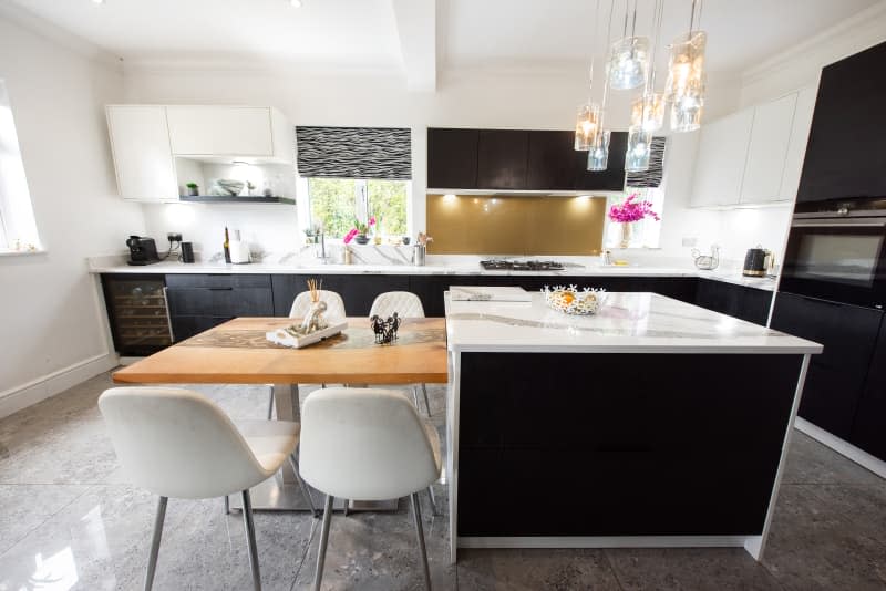 A general interior view of a large modern fitted kitchen diner, epoxy floor, painted white with black cabinets, marble effect quartz worktop, island and wooden dining table