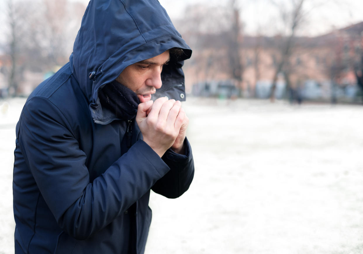Man breathing on his hands to keep them warm in outdoors snowy setting. (Getty Images)