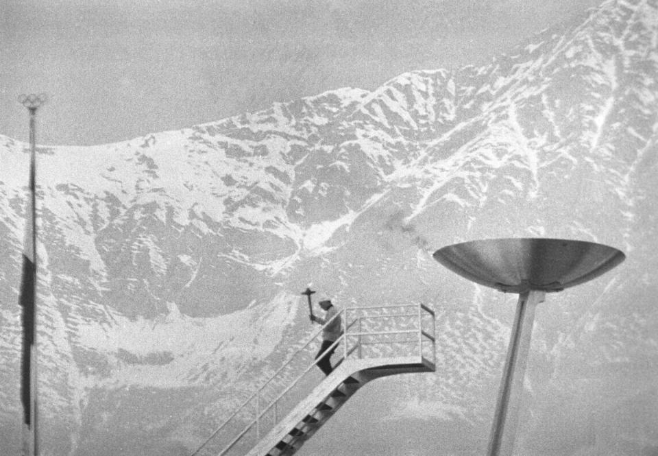 <p>After lighting the Olympic flame during the 1964 Winter Olympic Games in Austria, the torch bearer makes his way down a tall staircase against a stunning mountain landscape. </p>