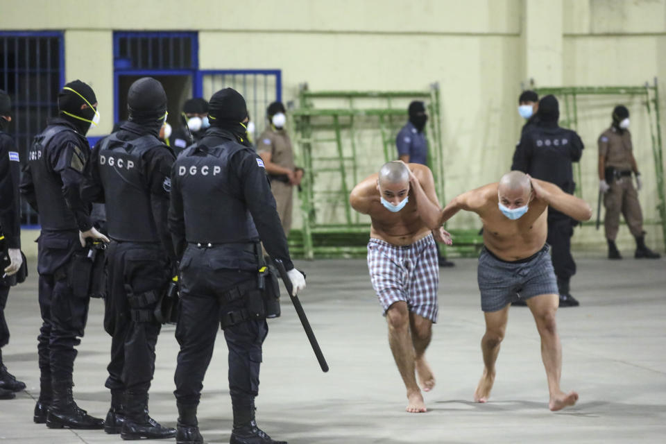 In this photo released by El Salvador Presidency Press Office police wearing masks as precautions against the new coronavirus guard inmates, also wearing masks, during a security operation after President Nayib Bukele decreed maximum emergency in prisons housing gang members at the Izalco prison in San Salvador, El Salvador, Saturday, April 25, 2020. Bukele ordered the emergency the day after more than twenty people were killed throughout country that authorities said were ordered from prisons. (El Salvador President Press Office via AP)