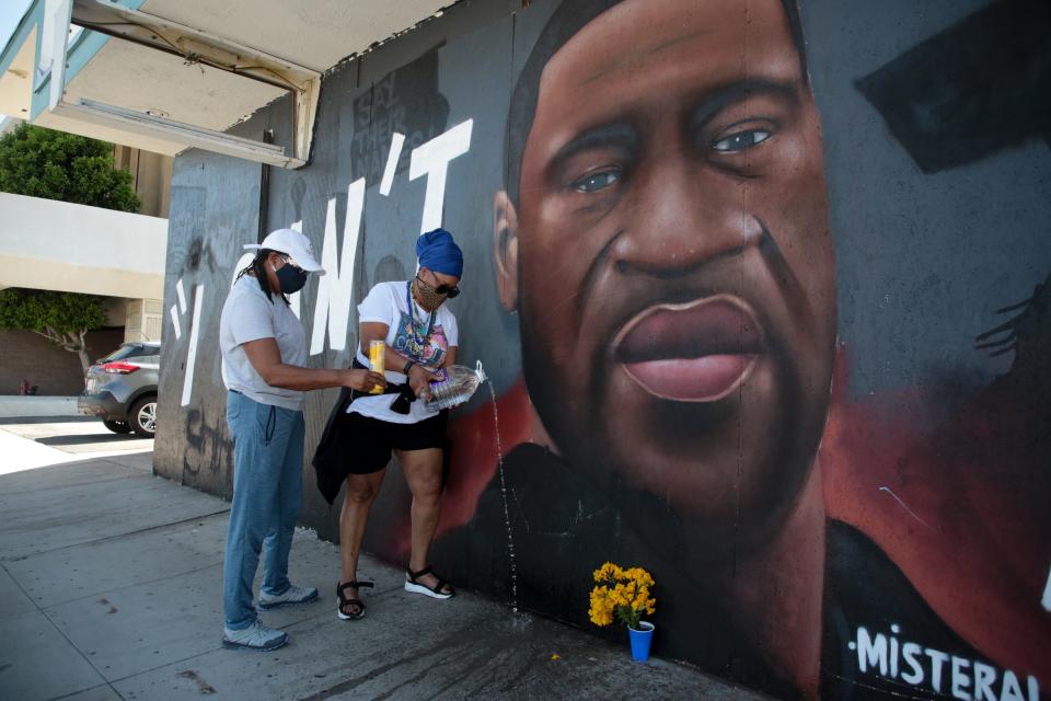 D Pepper Massey, left, and Asanti Love, right, light candles and pour water to honor George Floyd in front of the "I Can't Breathe" mural in downtown Palm Springs Tuesday.  Ex-police officer Derek Chauvin was convicted of killing Floyd minutes prior. The water is a symbol, Massey said, because "all life started in water."