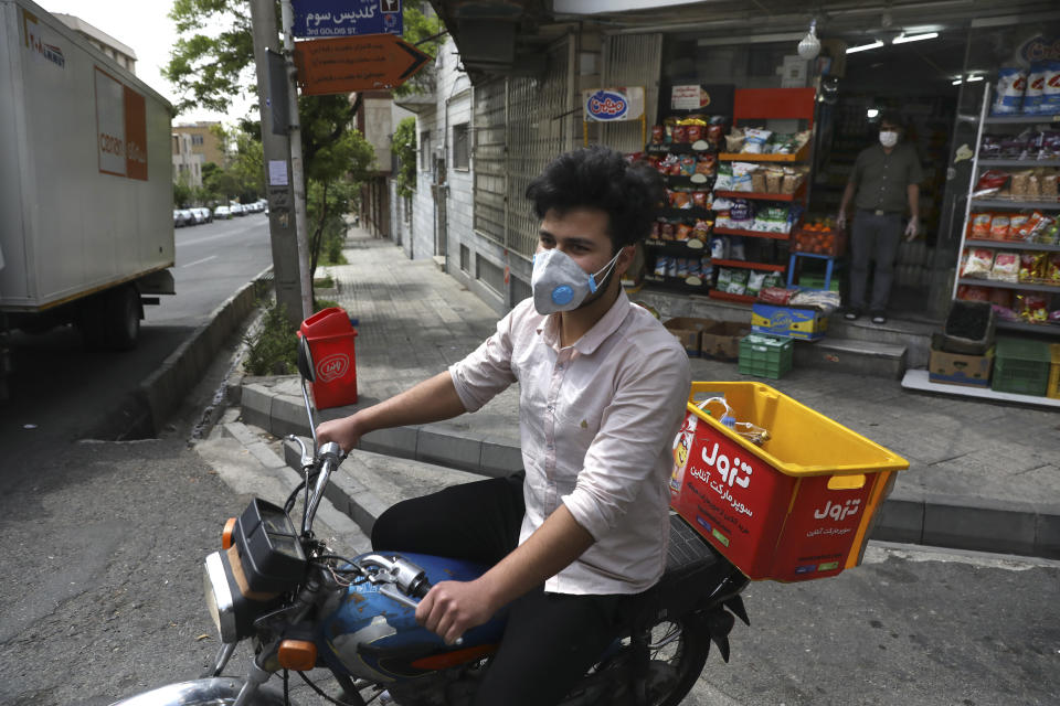In this Tuesday, April 21, 2020 photo, grocery delivery man Saeed Vatanparast, wearing a protective face mask to help prevent the spread of the coronavirus, leaves on his motorcycle for a delivery, in Tehran, Iran. For some $15 a day, deliverymen don masks and gloves in Iran's capital to zip across its pandemic-subdued streets to drop off groceries and food for those sheltering at home from the virus. (AP Photo/Vahid Salemi)