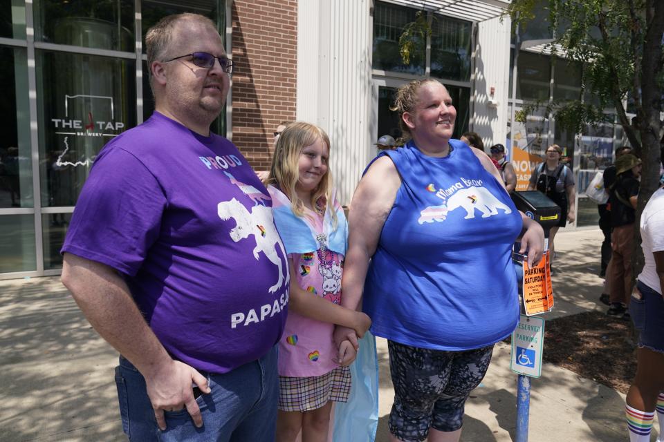 Flower Nichols, middle, watches the Pride Parade with her parents Kris and Jennilyn Nichols, Saturday, June 10, 2023, in Indianapolis. Families around the U.S. are scrambling to navigate new laws that prohibit their transgender children from accessing gender-affirming care. (AP Photo/Darron Cummings)