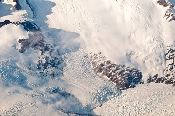 The heavily crevassed ice on this small Greenland outlet glacier cascades down to the fjord water (bottom right), which is filled with icebergs and small bits of ice.