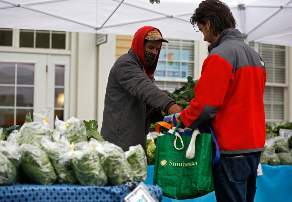 Adam Krein of Siembra Farm hands vegetables to a customer during the weekly Haile Farmers Market at Haile Village Center.