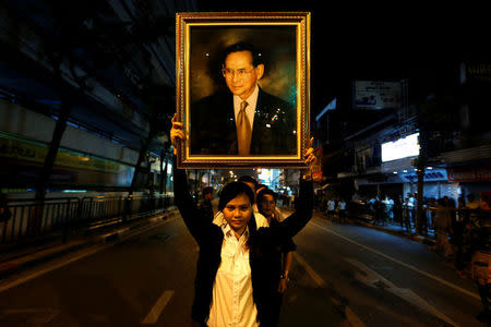 A woman poses with a portrait of Thailand's King Bhumibol Adulyadej, as others line up to hold the portrait, after the announcement of the king's death, outside Siriraj hospital in Bangkok, Thailand October 13, 2016. REUTERS/Jorge Silva