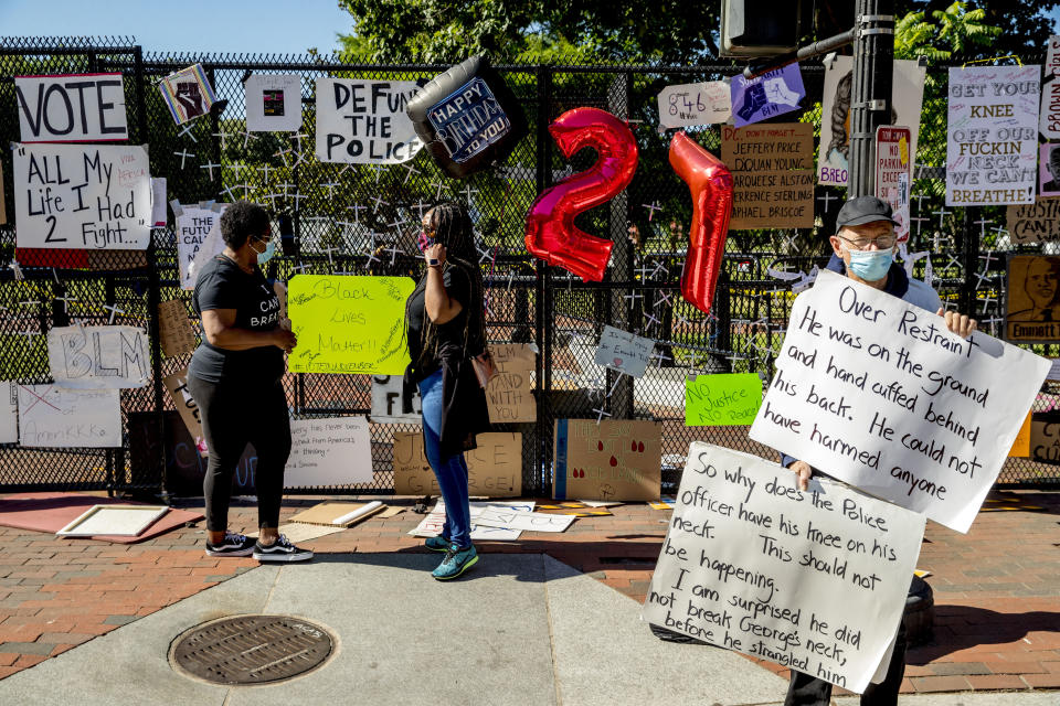 People stop to look at signs on a security fence at 16th and H Street, Monday, June 8, 2020, in Washington, after days of protests over the death of George Floyd, a black man who was in police custody in Minneapolis. Floyd died after being restrained by Minneapolis police officers. (AP Photo/Andrew Harnik)