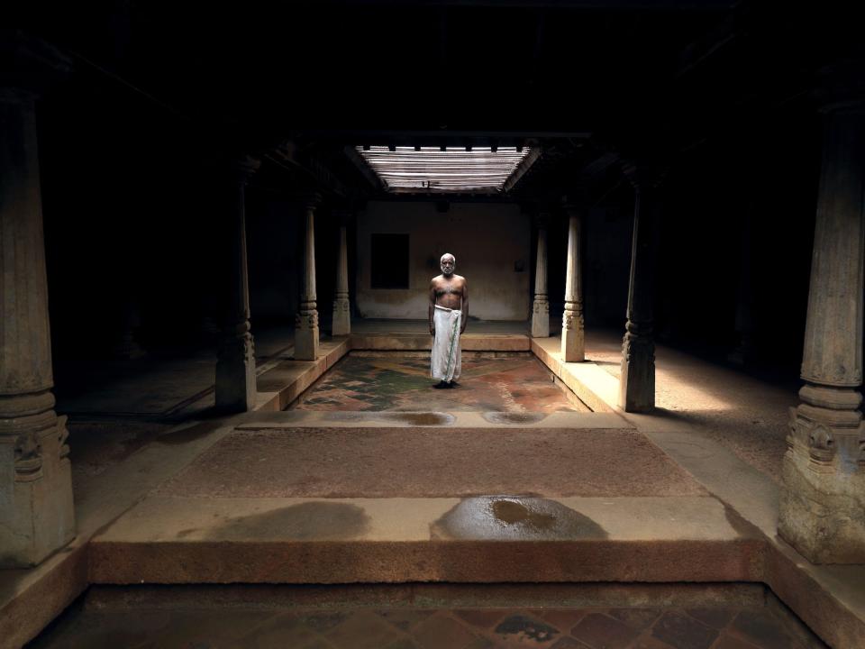 A man stands in an open area of the mansion where he lives.