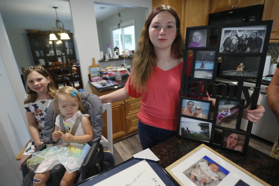 FILE - Morgan Nixon, right, poses with her sisters, Mackenzie, left, Madilyn, second from left, as they display memorabilia at their home Friday May 22, 2020, in Virginia Beach, Va, from the 2019 shooting that took the life of their mom Kate Nixon. A state commission tasked with investigating the 2019 mass shooting in Virginia Beach has called for numerous changes to how Virginia and its communities respond to mass shootings. (AP Photo/Steve Helber, File)