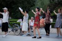 An elderly man rests as residents dance during their daily exercise at a city square in Weifang