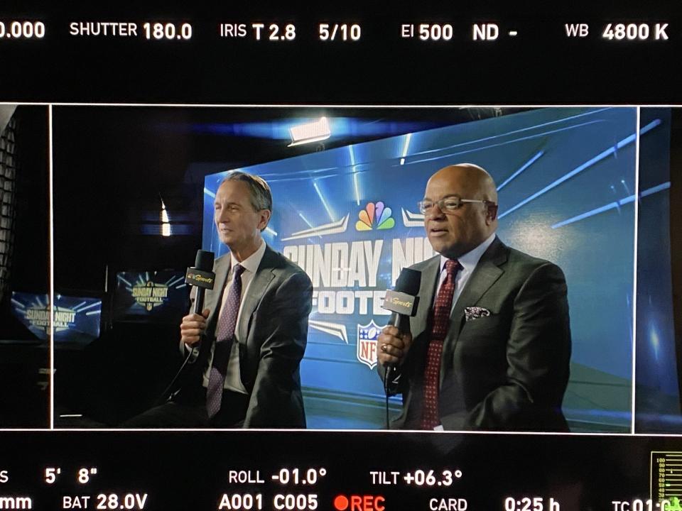 Mike Tirico and Chris Collinsworth pictured in the frame of a live camera feed during a Sunday Night Football broadcast.