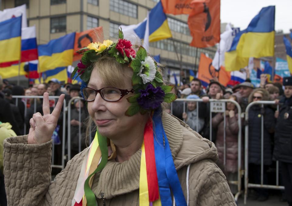 An elderly woman dressed in a Ukrainian folk costume shows V-sing as demonstrators hold Russian and Ukrainian flags during a massive rally to oppose president Vladimir Putin's policies in Ukraine, in Moscow, Saturday, March 15, 2014. Large rival marches have taken place in Moscow over Kremlin-backed plans for Ukraine’s province of Crimea to break away and merge with Russia. More than 10,000 people turned out Saturday for a rally in the center of the city held to oppose what many demonstrators described as Russia’s invasion of the Crimean Peninsula. In a nearby location, a similar sized crowd voiced its support for Crimea’s ethnic Russian majority, who Moscow insists is at threat from an aggressively nationalist leadership now running Ukraine. (AP Photo/Alexander Zemlianichenko)