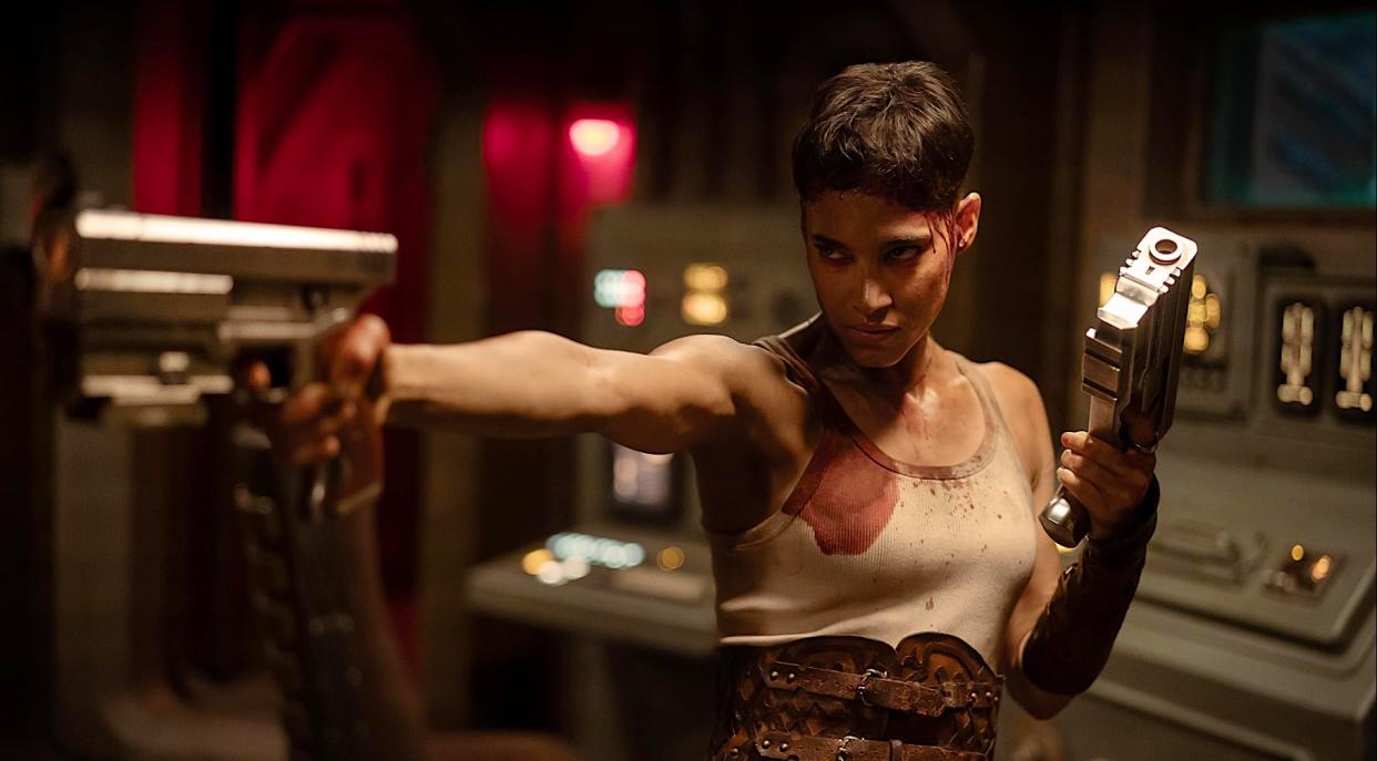  A tough woman in a tank top prepares to fire two space pistols. 
