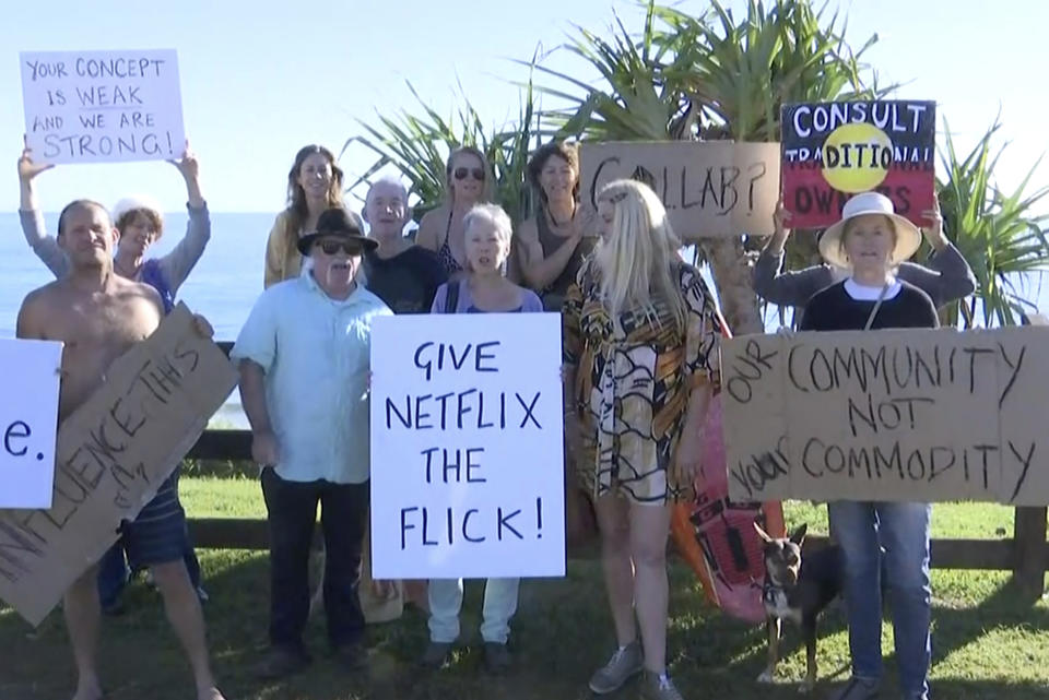 In this image made from video, protesters display placards at Byron Bay, Australia, Tuesday, April 20, 2021. Angry Byron Bay locals are protesting the filming of a reality television series that some fear will damage the reputation of their trendy Australian tourist town. Netflix says its first Australian reality series would “aim to build a connection between the people we meet in the show and the audience.” (Australian Broadcasting Corporation via AP)