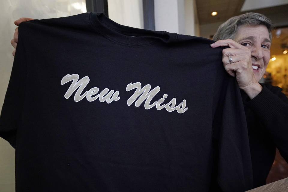 Suzi Altman holds a "New Miss" shirt, Nov. 23, 2021, in Jackson, Miss. The shirt and hats she produces, uses the same the cursive script as the Ole Miss logo that appears on football helmets, sports jerseys, marketing materials and all manner of bags, clothing and other merchandise licensed by the University of Mississippi. Altman applied for the New Miss trademark in July 2020, but the school has filed papers trying to block her from trademarking the "New Miss" logo. (AP Photo/Rogelio V. Solis)