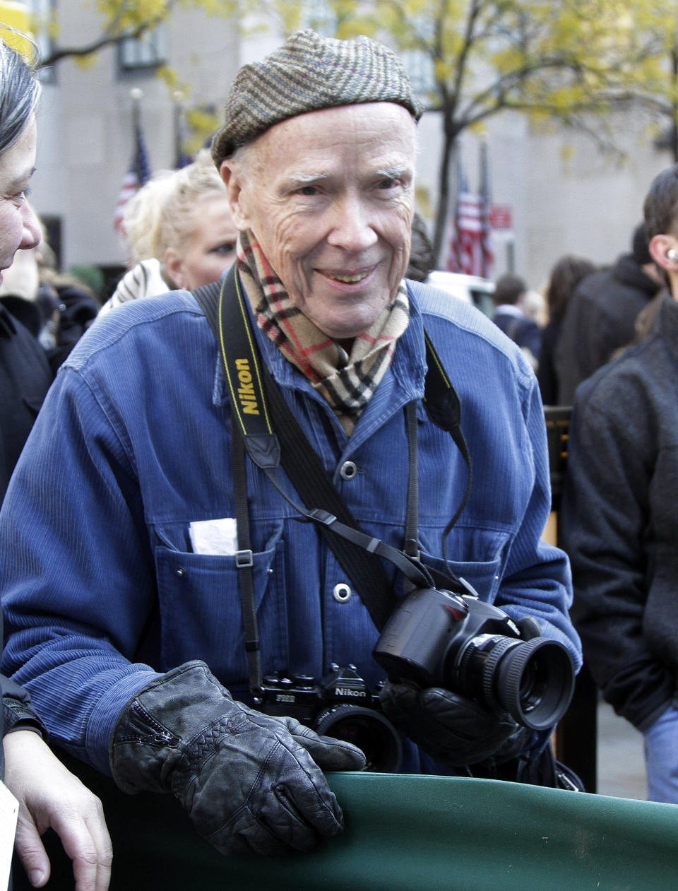 In this Nov. 11, 2011 file photo, New York Times photographer Bill Cunningham waits for the arrival of the annual Rockefeller Center Christmas tree, in New York. Cunningham’s project of 88 prints, “Facades,” is being featured in an exhibition at the New-York Historical Society, running through June 15, 2014. Long before his images of street fashion became a regular newspaper feature, Cunningham spent eight years, from 1968 to 1976, working on the whimsical photo essay of models in period costumes posing against historic sites of the same vintage. (AP Photo/Richard Drew, File)