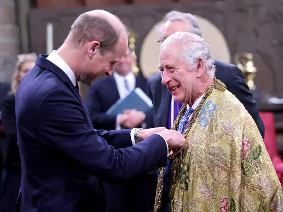 King Charles laughs as Prince William pins something to his chest.