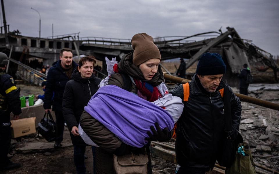 A woman carrying her baby crosses a destroyed bridge as they flee the city of Irpin - DIMITAR DILKOFF/AFP
