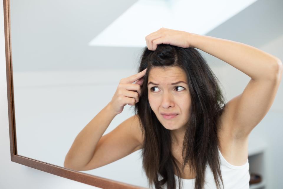 Woman looking in the mirror at her scalp.