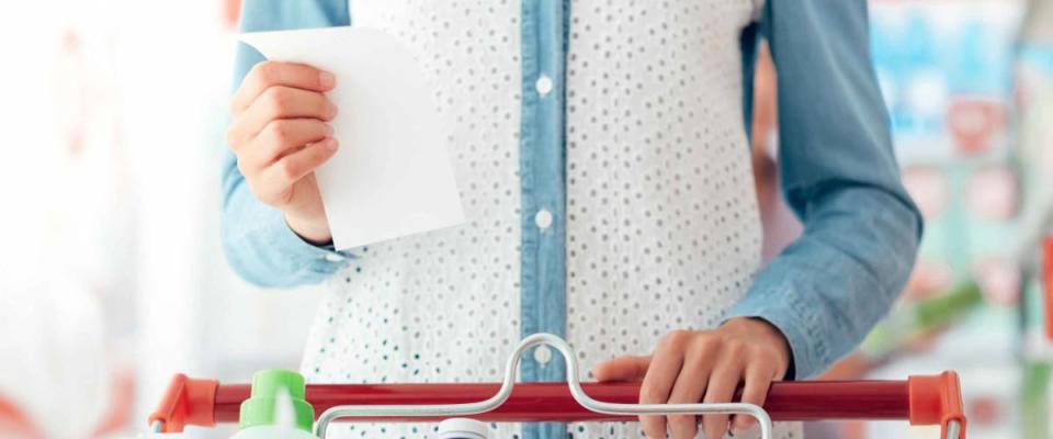 Woman doing grocery shopping at the supermarket, she is pushing a cart and checking a list