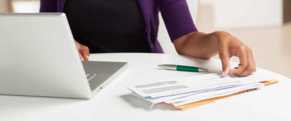 Attractive young African American woman working on finances at home wearing purple jacket sitting at dining table.