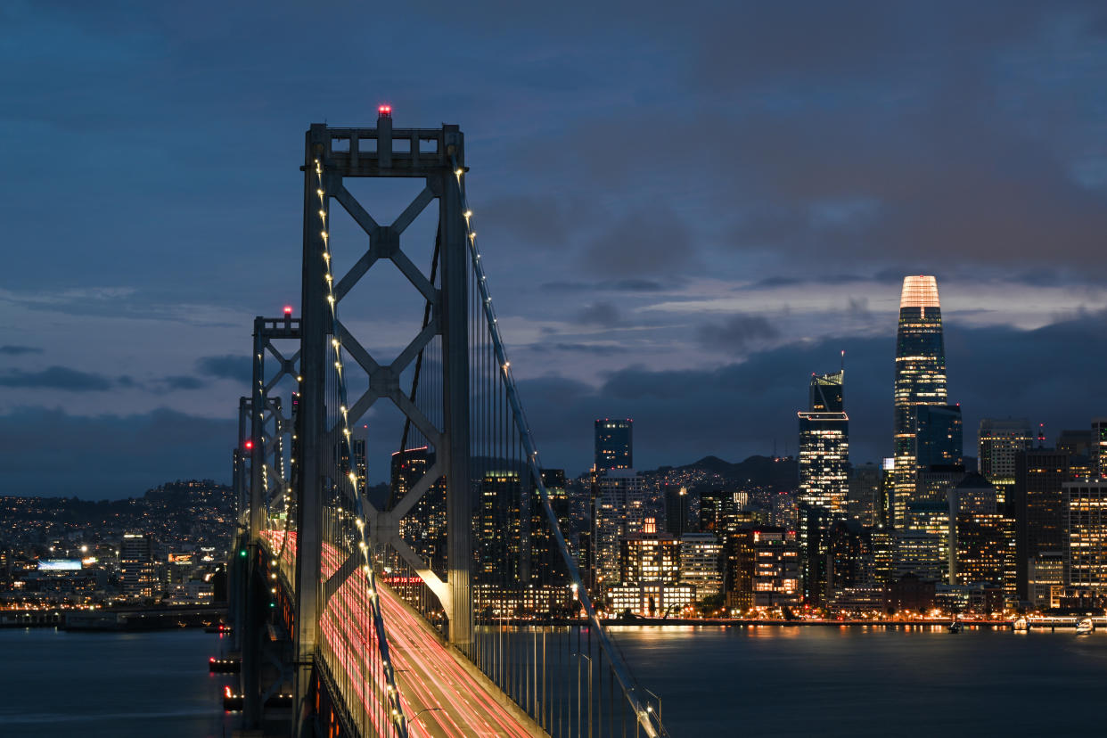 The San Francisco Bay Bridge looking over to the city skyline, dominated by the Salesforce Tower, whose top stories are lit up.