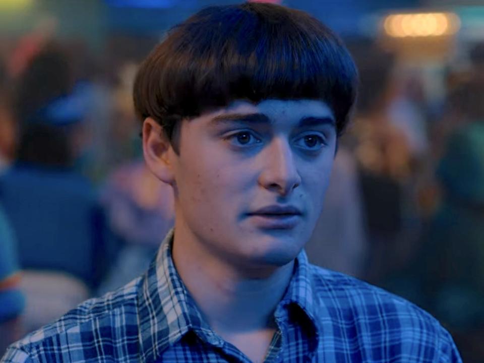 A teenage boy with a bowl cut and plaid shirt looks sad.