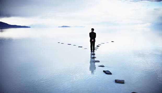 Businessman at fork of stone pathway in water