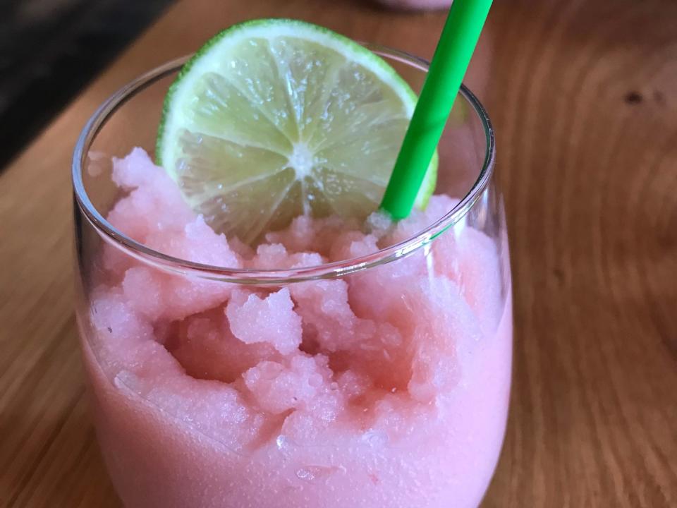 Ein Glas Frosé mit einer Limettenscheibe und einem grünen Strohhalm